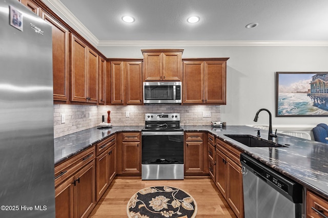 kitchen with appliances with stainless steel finishes, a sink, ornamental molding, dark stone counters, and light wood-type flooring