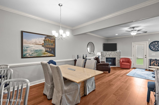 dining area with wood finished floors, crown molding, a stone fireplace, a chandelier, and a ceiling fan