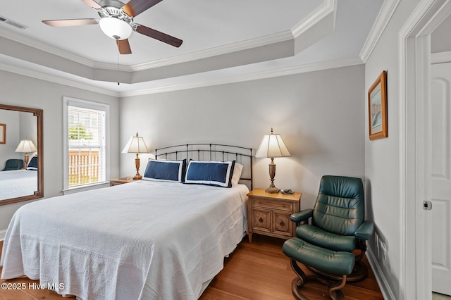 bedroom with wood finished floors, a tray ceiling, crown molding, ceiling fan, and baseboards