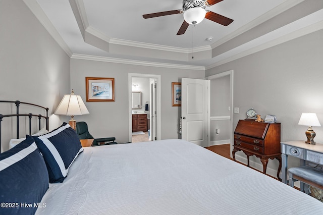 bedroom with a tray ceiling, crown molding, ensuite bath, wood finished floors, and baseboards
