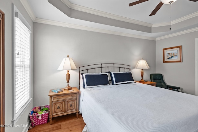 bedroom with wood finished floors, a tray ceiling, ornamental molding, and ceiling fan