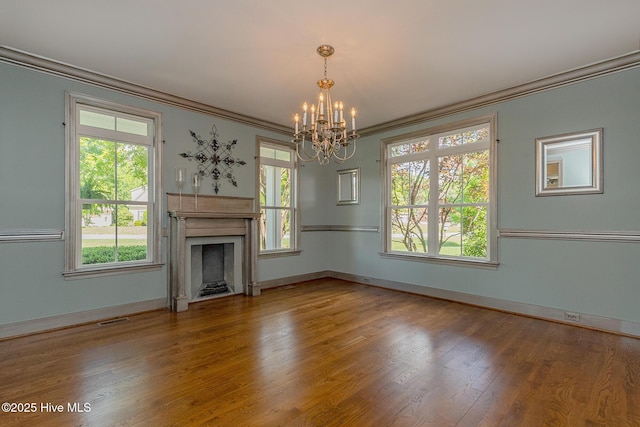 unfurnished living room featuring crown molding, a chandelier, a fireplace, wood finished floors, and healthy amount of natural light