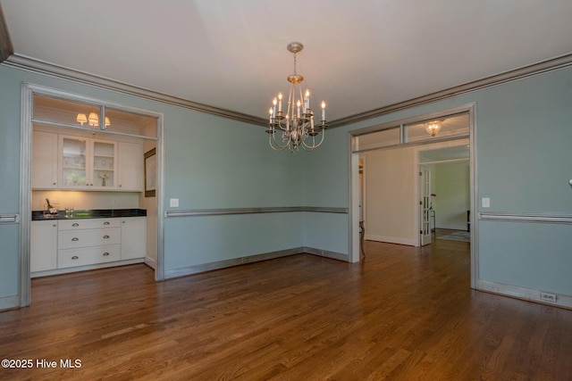 spare room featuring a chandelier, ornamental molding, dark wood-style flooring, baseboards, and a bar
