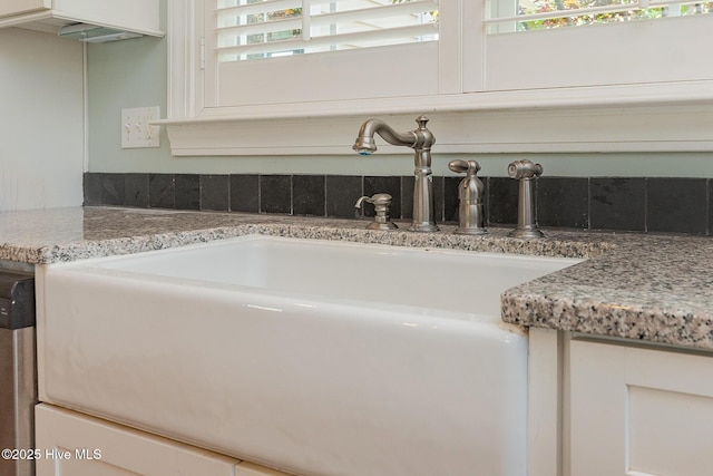 detailed view of a sink, white cabinetry, and light stone counters