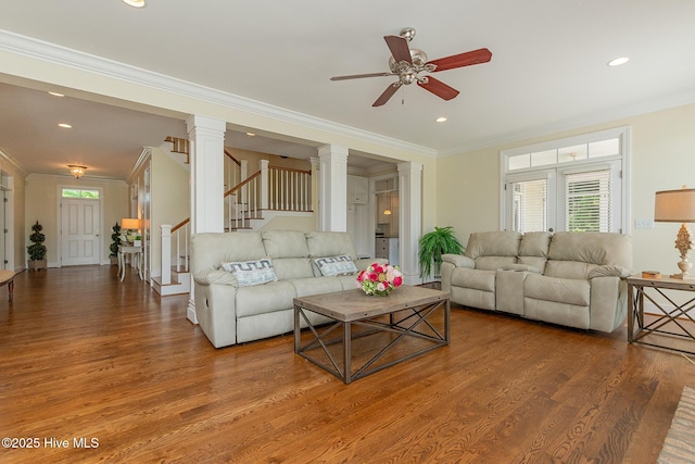 living area featuring crown molding, wood finished floors, ceiling fan, ornate columns, and stairs