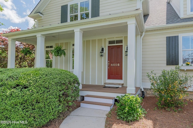 view of exterior entry with a shingled roof and covered porch
