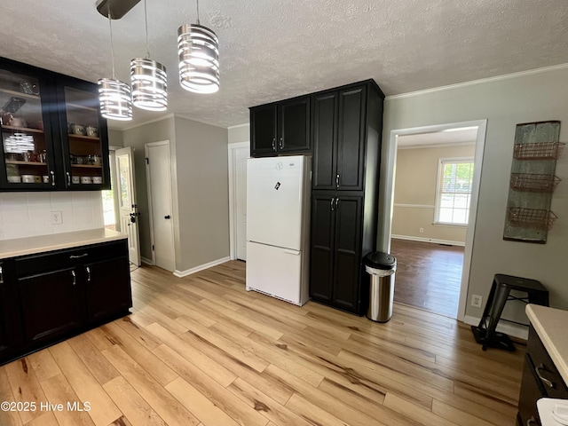 kitchen featuring freestanding refrigerator, ornamental molding, baseboards, light wood-style floors, and dark cabinets