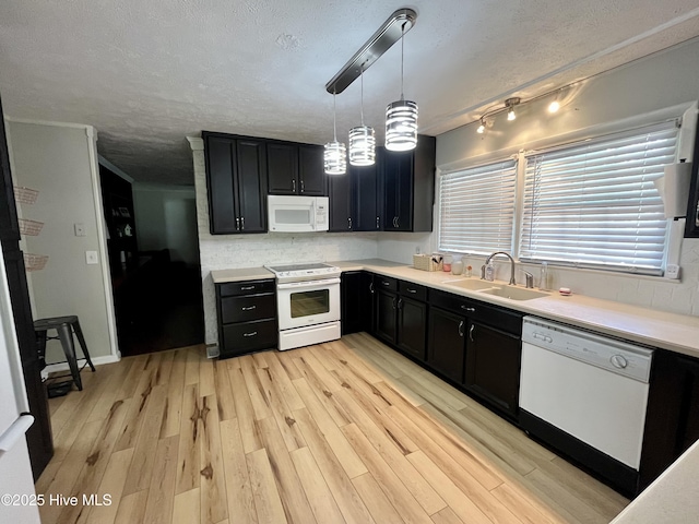 kitchen featuring white appliances, a sink, dark cabinetry, a textured ceiling, and light wood-style flooring