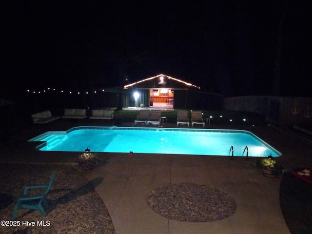 pool at night featuring a patio and an outdoor pool