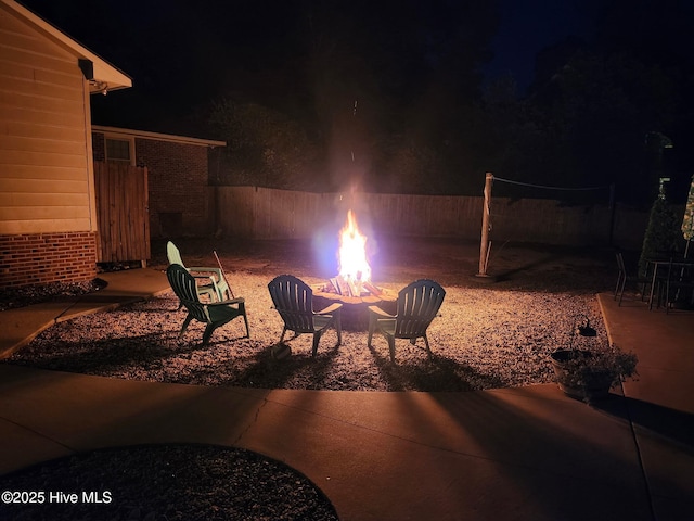 patio at night featuring a fire pit and fence