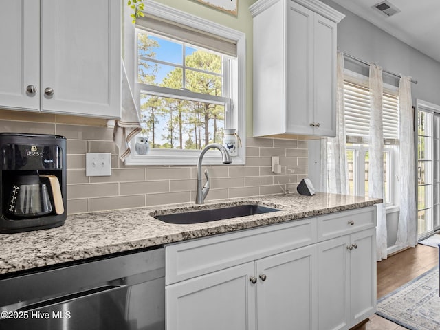 kitchen featuring dishwasher, a sink, white cabinets, and backsplash