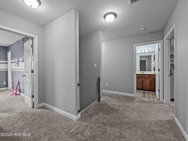 hall featuring carpet floors, baseboards, a sink, and an upstairs landing