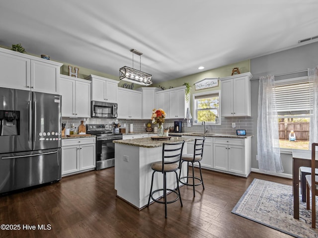 kitchen with appliances with stainless steel finishes, a kitchen island, white cabinetry, backsplash, and a sink