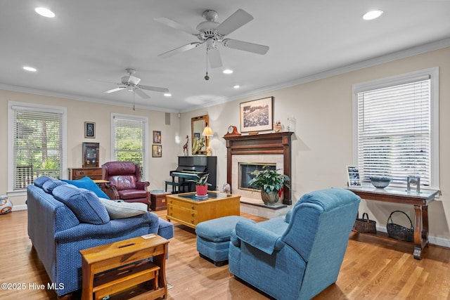 living room featuring light wood-type flooring, a high end fireplace, crown molding, recessed lighting, and ceiling fan