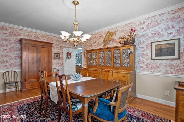 dining room featuring wallpapered walls, wainscoting, a chandelier, wood finished floors, and crown molding