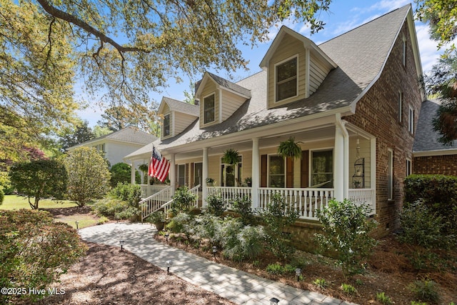 cape cod-style house featuring covered porch, roof with shingles, and brick siding