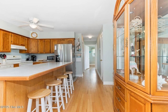 6301 Ocean Dr, Emerald Isle, NC 28594 - kitchen with stainless steel appliances, under cabinet range hood, light wood-type flooring, brown cabinets, and light countertops