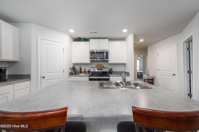 kitchen featuring appliances with stainless steel finishes, a sink, a breakfast bar, white cabinetry, and an island with sink
