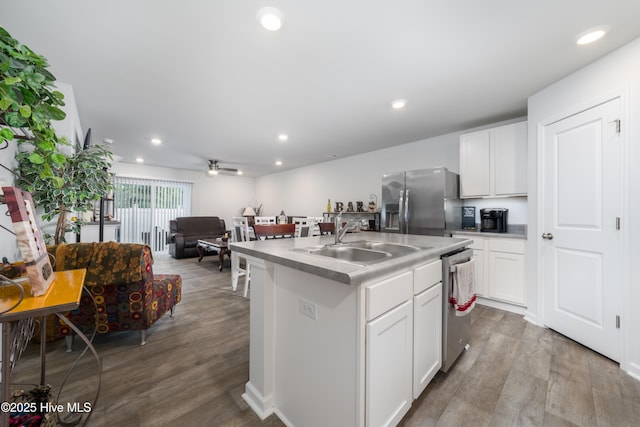 kitchen with stainless steel appliances, a sink, open floor plan, wood finished floors, and white cabinetry