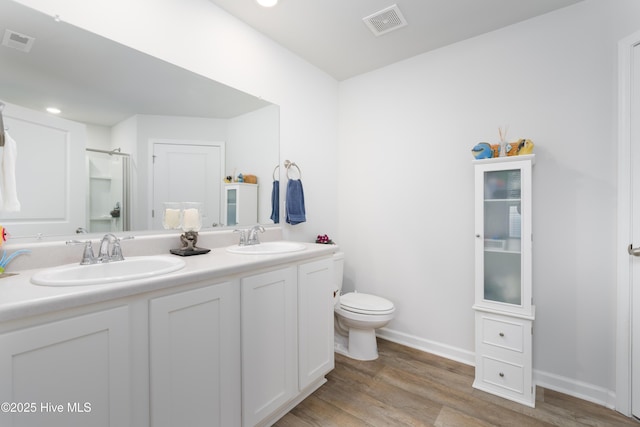 full bath with wood finished floors, a shower with door, double vanity, toilet, and baseboards