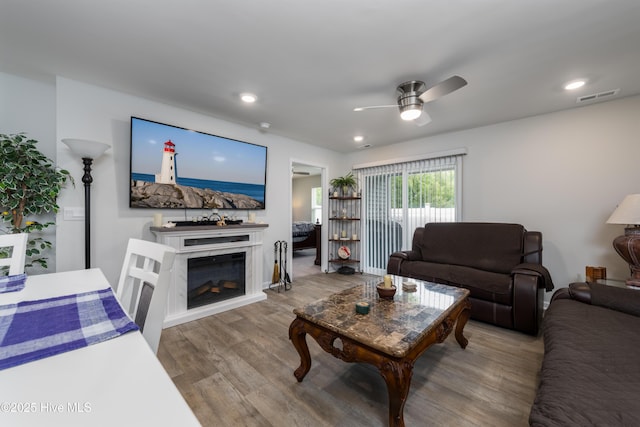 living room with wood finished floors, a ceiling fan, a glass covered fireplace, and recessed lighting
