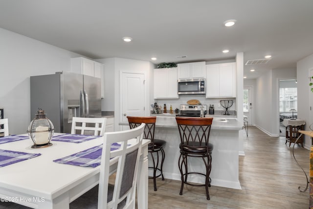 kitchen with stainless steel appliances, white cabinetry, light wood finished floors, a kitchen breakfast bar, and a kitchen island