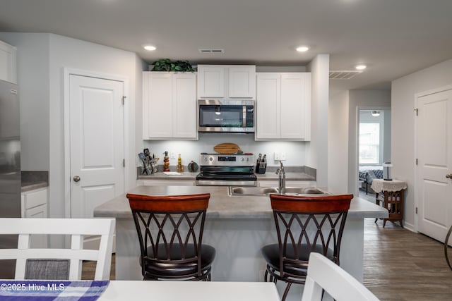 kitchen with appliances with stainless steel finishes, a sink, white cabinetry, dark wood-type flooring, and recessed lighting