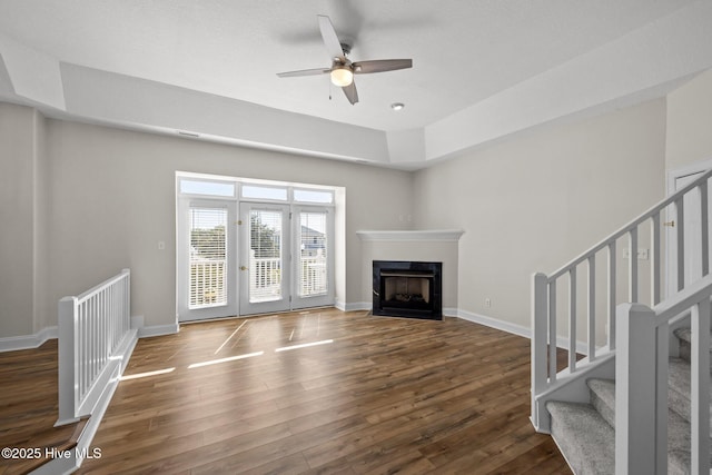 unfurnished living room with wood finished floors, a ceiling fan, baseboards, and stairs
