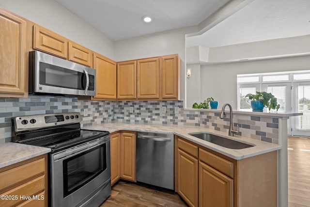 kitchen featuring appliances with stainless steel finishes, a sink, a peninsula, light stone counters, and recessed lighting
