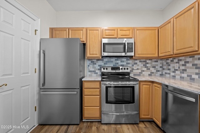 kitchen with appliances with stainless steel finishes, decorative backsplash, light stone countertops, and wood finished floors