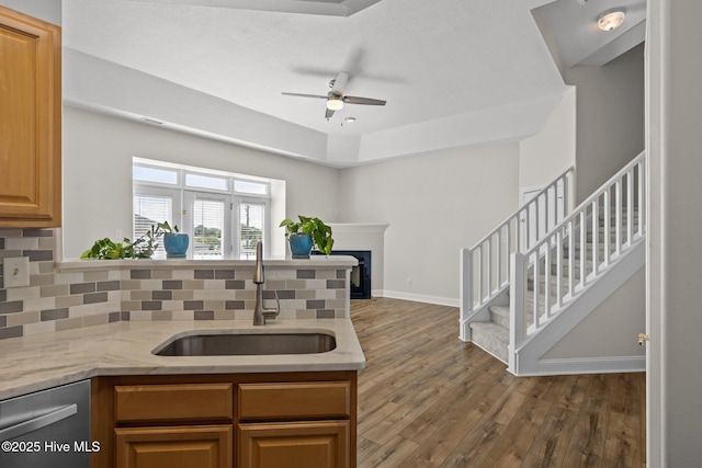 kitchen with a sink, wood finished floors, ceiling fan, stainless steel dishwasher, and decorative backsplash