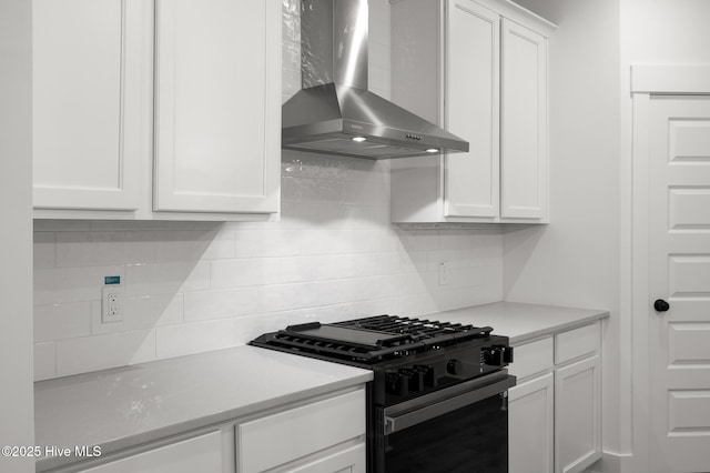kitchen featuring black gas range, wall chimney exhaust hood, decorative backsplash, white cabinets, and light countertops