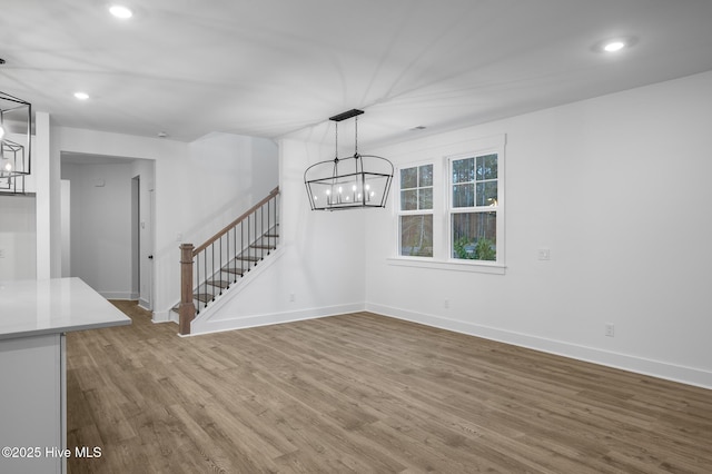 unfurnished living room featuring a chandelier, stairs, wood finished floors, baseboards, and recessed lighting