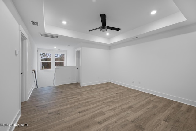 spare room with a raised ceiling, recessed lighting, wood finished floors, ceiling fan, and baseboards