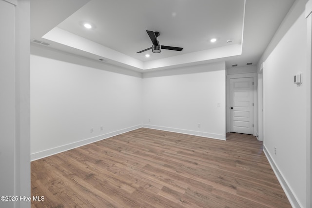 unfurnished room with a raised ceiling, a ceiling fan, recessed lighting, wood finished floors, and baseboards