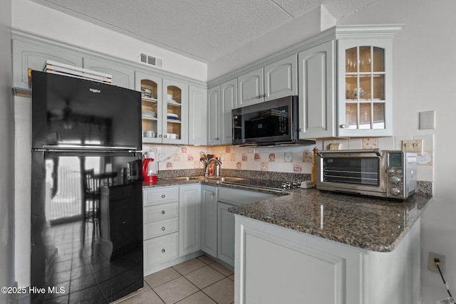 kitchen with freestanding refrigerator, a sink, dark stone counters, glass insert cabinets, and a textured ceiling