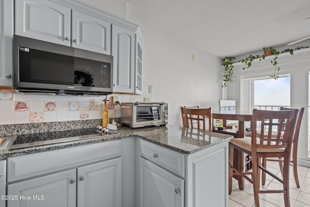 kitchen featuring stainless steel microwave, black electric stovetop, backsplash, dark stone countertops, and a textured ceiling
