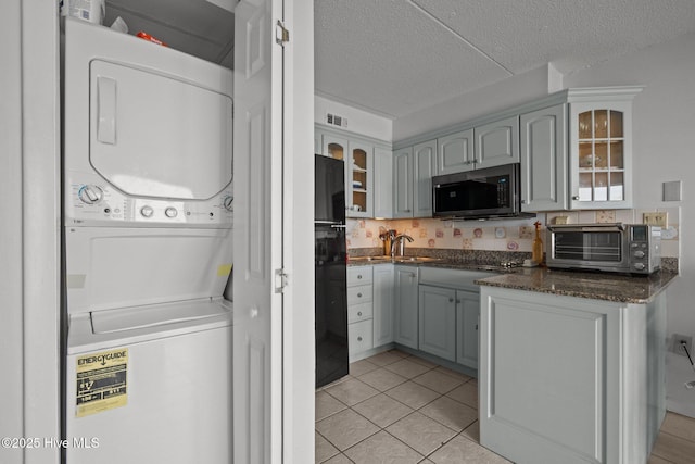 kitchen with stacked washer / drying machine, stainless steel microwave, freestanding refrigerator, glass insert cabinets, and a textured ceiling