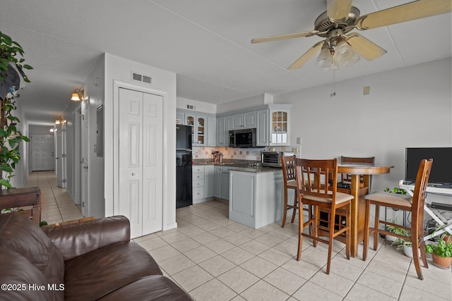 kitchen featuring stainless steel microwave, light tile patterned floors, glass insert cabinets, dark countertops, and ceiling fan