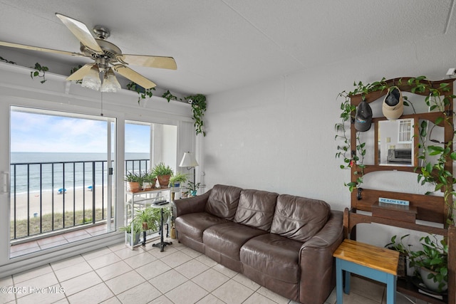 living area featuring ceiling fan, light tile patterned floors, and view of water and beach