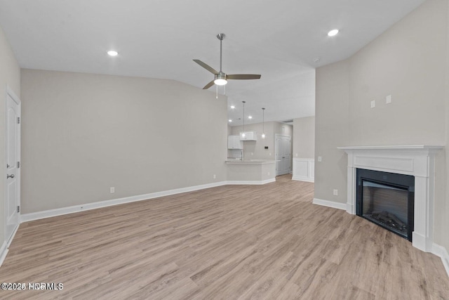 unfurnished living room featuring vaulted ceiling, ceiling fan, light wood-style flooring, baseboards, and a glass covered fireplace