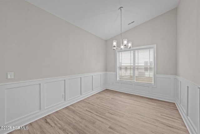 unfurnished dining area featuring a chandelier, a wainscoted wall, lofted ceiling, light wood-style flooring, and a decorative wall