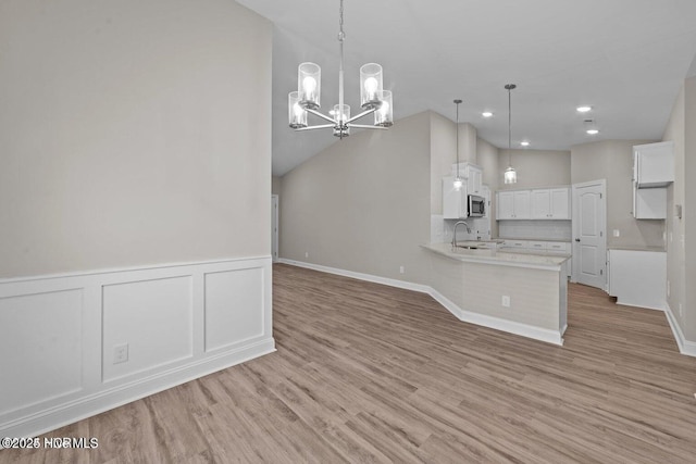 kitchen featuring a sink, a chandelier, stainless steel microwave, white cabinetry, and a peninsula