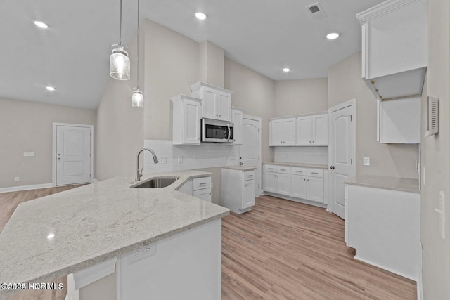 kitchen featuring stainless steel microwave, a sink, a peninsula, light stone countertops, and backsplash