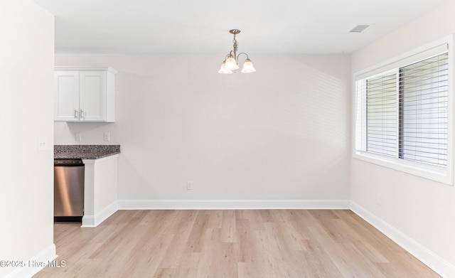 unfurnished dining area with light wood-style flooring, a chandelier, and baseboards