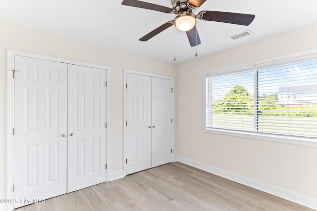 unfurnished bedroom featuring multiple closets, light wood-style floors, baseboards, and ceiling fan