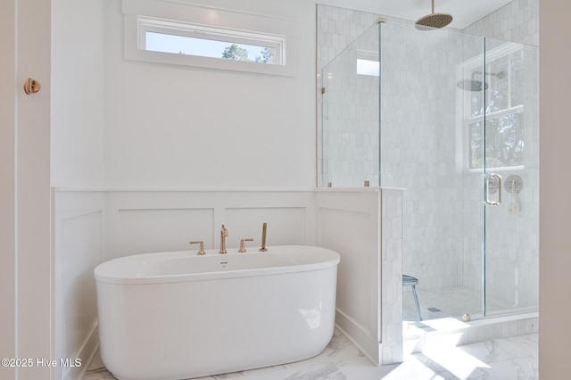 full bathroom with marble finish flooring, a decorative wall, a shower stall, a soaking tub, and wainscoting