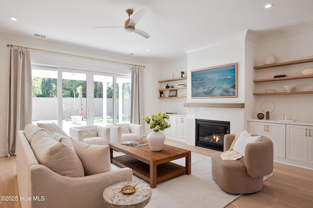 living room with light wood-style floors, ornamental molding, a glass covered fireplace, a ceiling fan, and recessed lighting