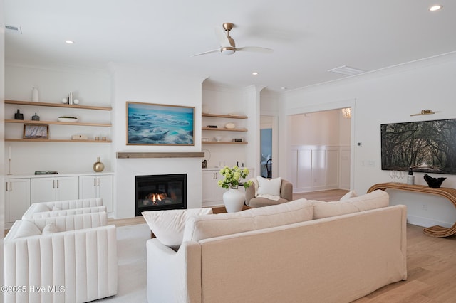 living room with ornamental molding, a ceiling fan, light wood finished floors, a glass covered fireplace, and recessed lighting