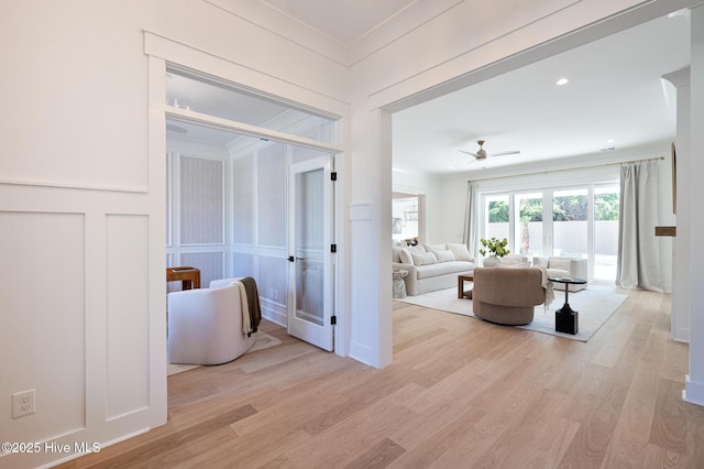 hall featuring a decorative wall, light wood finished floors, and crown molding